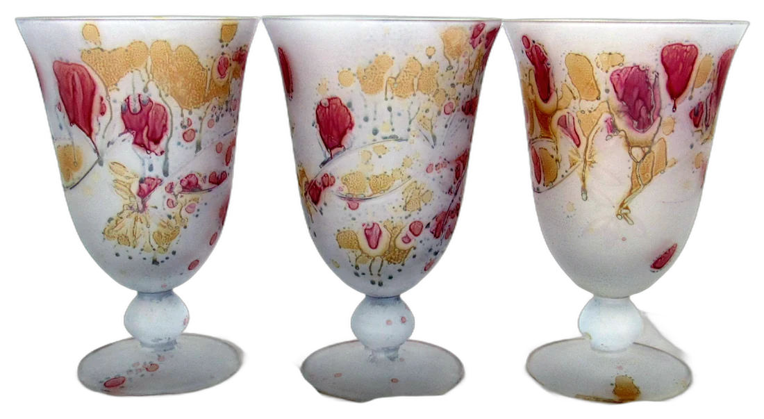 Tres copas de vidrio blanco con flores rosadas y doradas