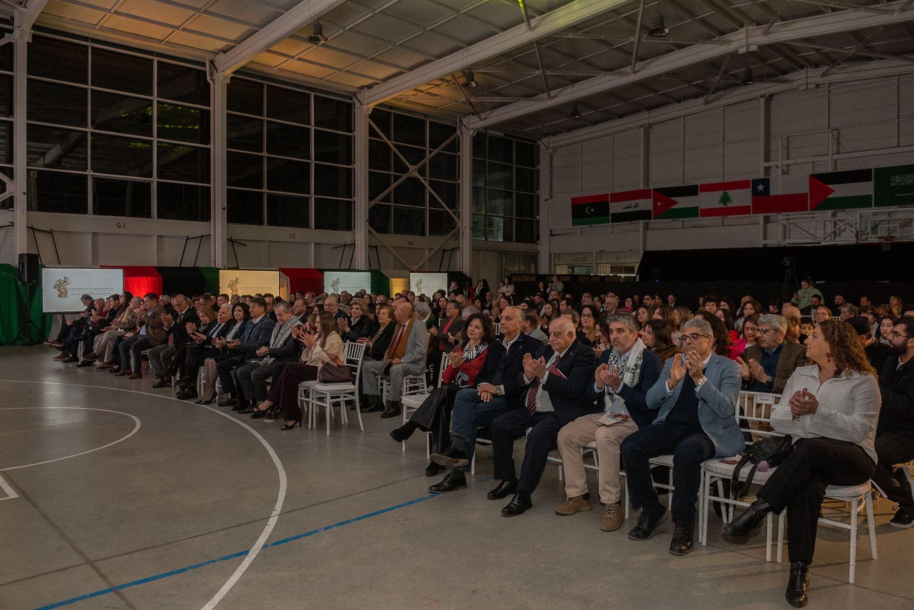 Público sentado frente al escenario, bajo una fila de banderas