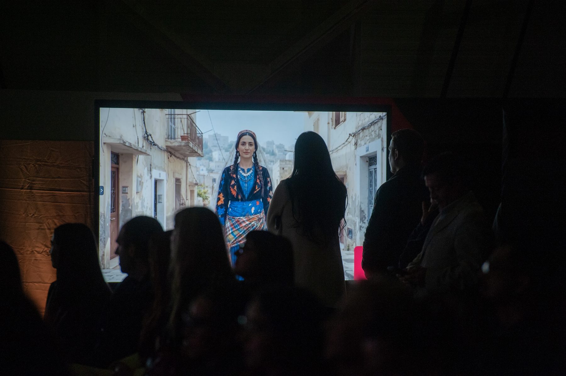 El público mira una proyección con mujeres vestidas con trajes palestinos