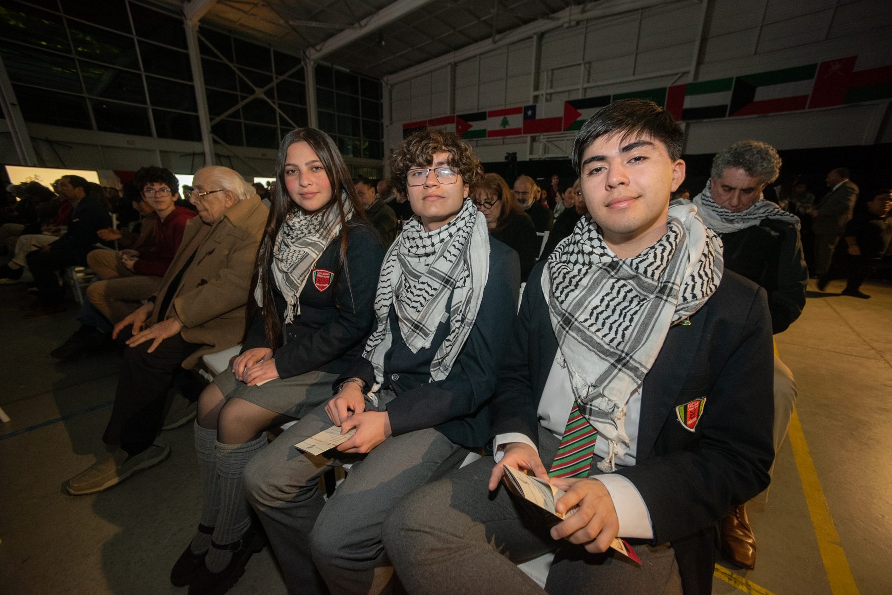 Estudiantes de uniforme con kufiya sentados entre el público