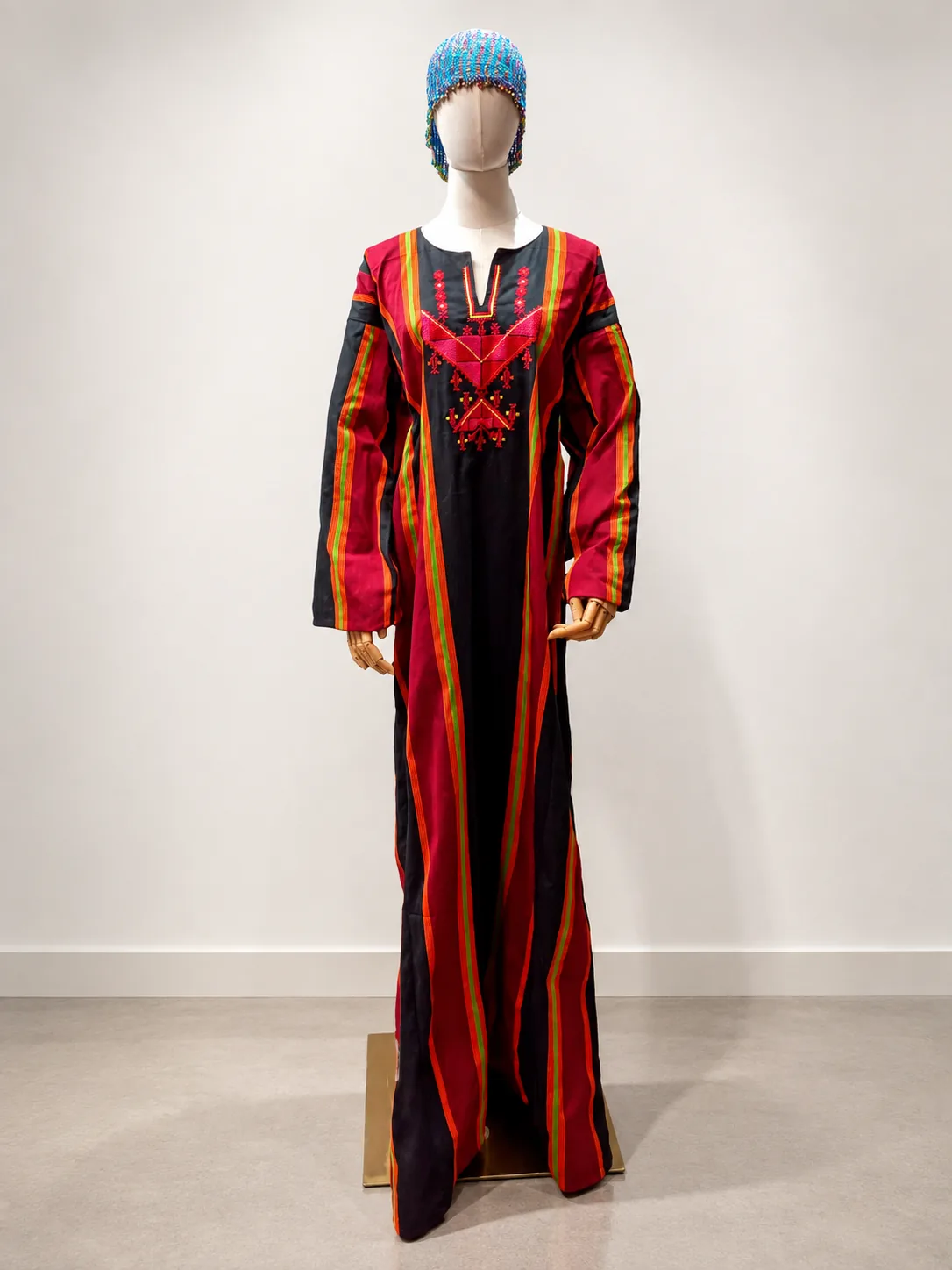 Vestido de listas rojas, magenta y negras con cofia azul, sobre maniquí