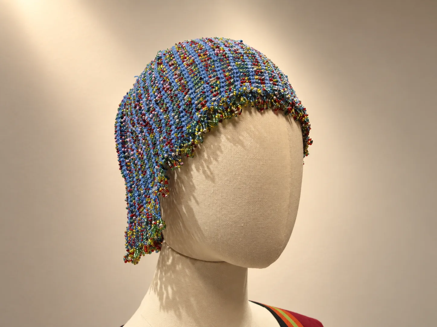 Cofia de malla azul con cuentas de colores sobre una cabeza de maniquí